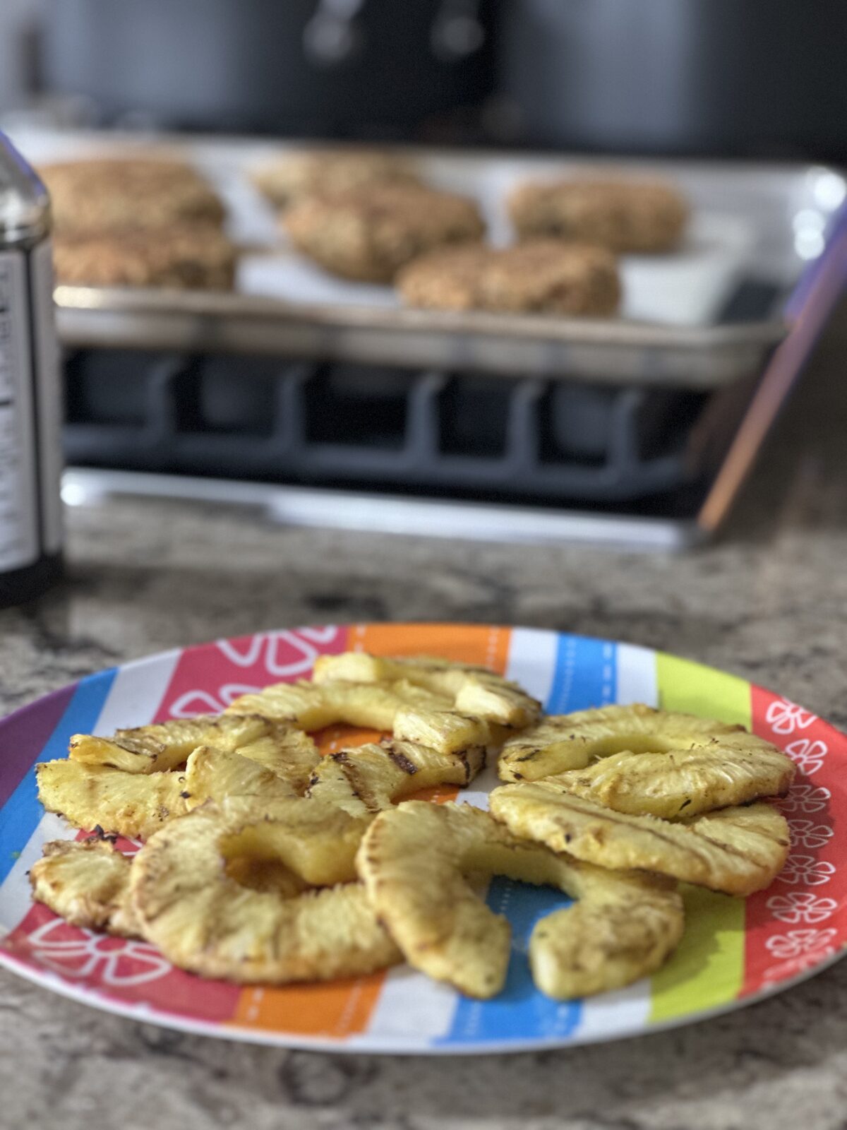 Grilled pineapple rings on a colorful plate with veggie burger patties in the background