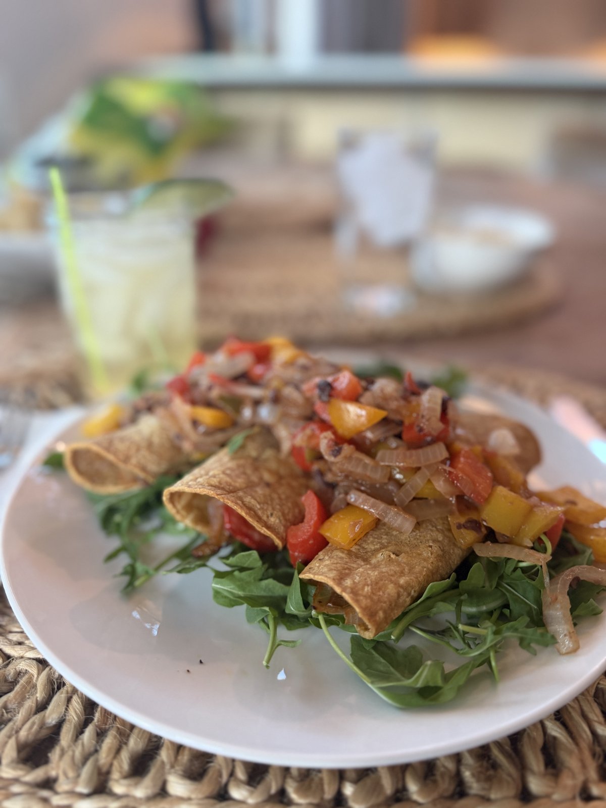 Crisp baked taquitos on a bed of fresh arugula, topped with sautéed red, yellow, and orange bell peppers and onions