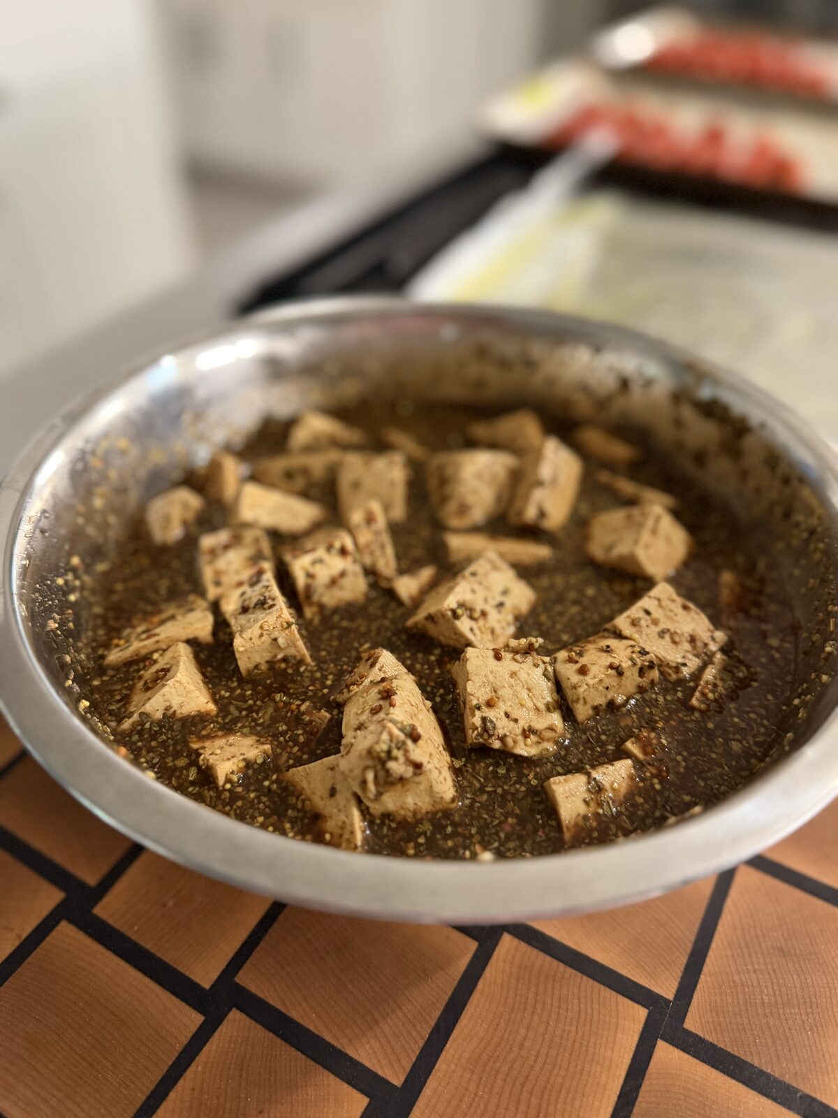 Cubes of tofu marinating in a skillet of dark, herb-flecked marinade